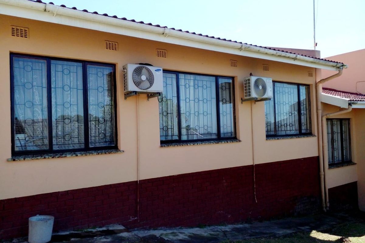 Rear exterior view of the house featuring brick plinth, security bars on windows, and wall-mounted air conditioning units.
