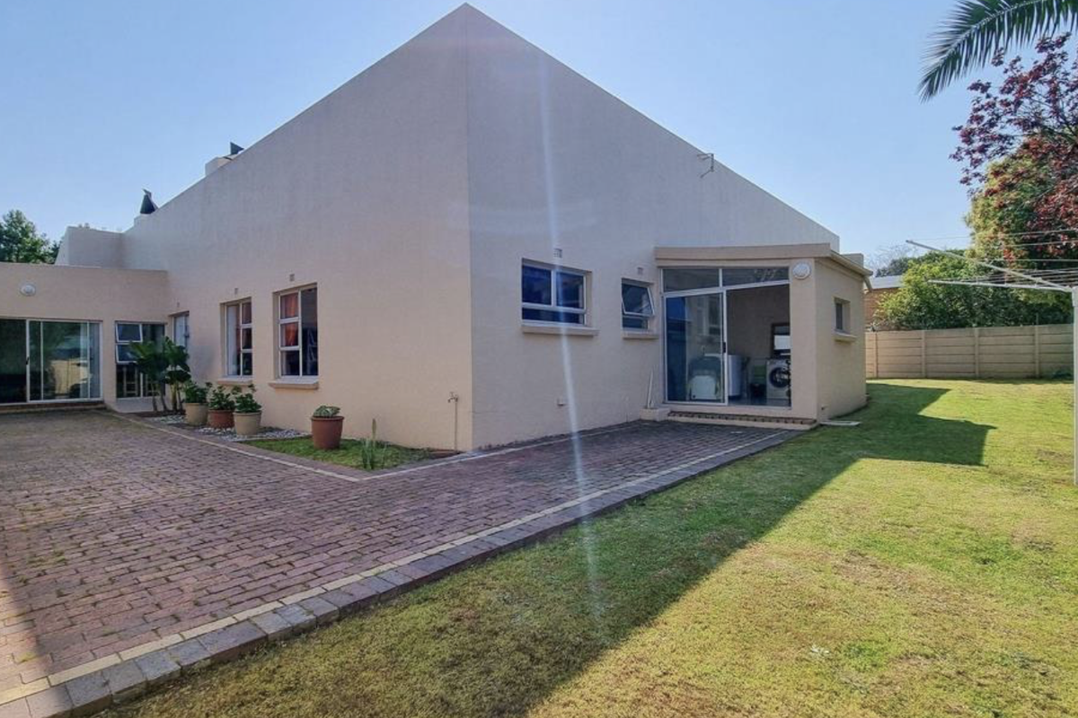 Rear view of the property featuring a paved patio area, sliding glass doors, and a well-maintained garden with boundary walling.