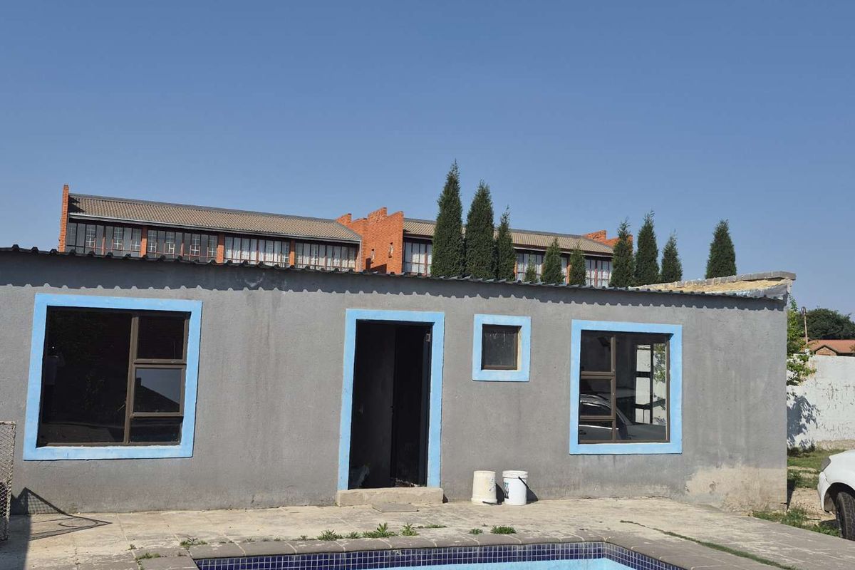 Rear exterior view of the property featuring a swimming pool, concrete patio area, and a single-story structure with aluminium window frames.