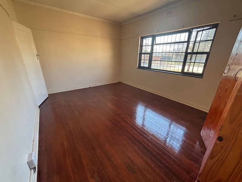 An empty bedroom featuring polished hardwood flooring, a large window with security bars, and classic picture rail detailing.