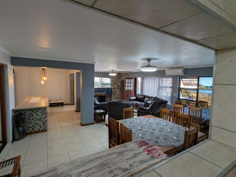 Spacious open-plan living and dining area featuring tiled floors, a breakfast bar, stone feature wall, and split system air conditioning.