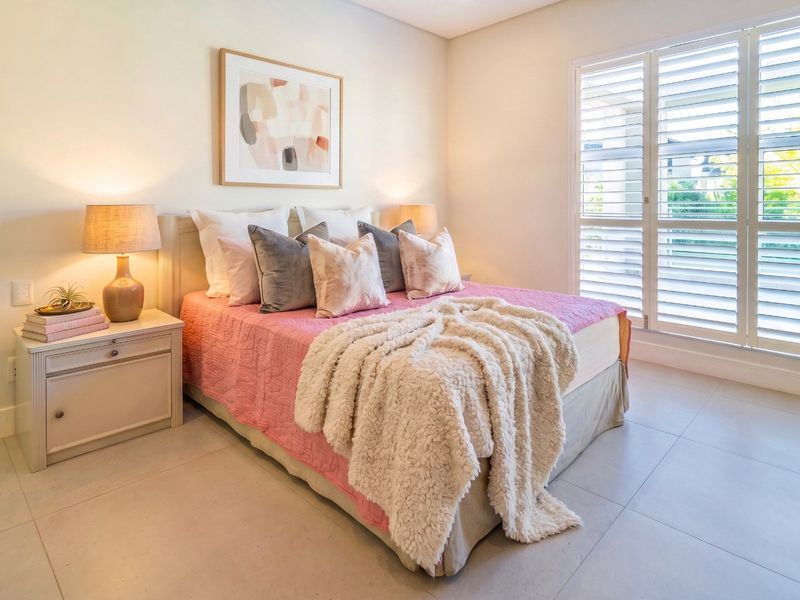 A bright and well-maintained bedroom featuring neutral tiled flooring and white plantation shutters, offering a clean and comfortable living space.