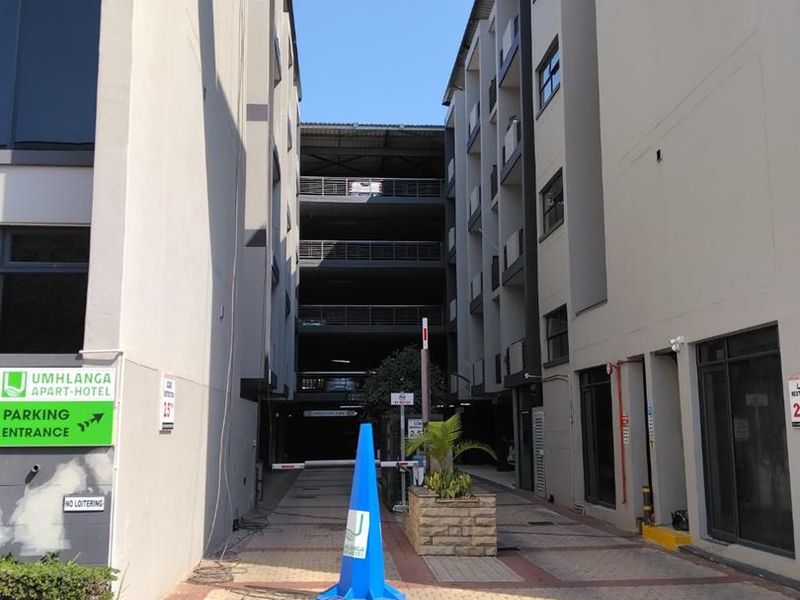 View of the entrance to the Umhlanga Apart-Hotel, featuring a paved driveway leading to a multi-level parking structure.