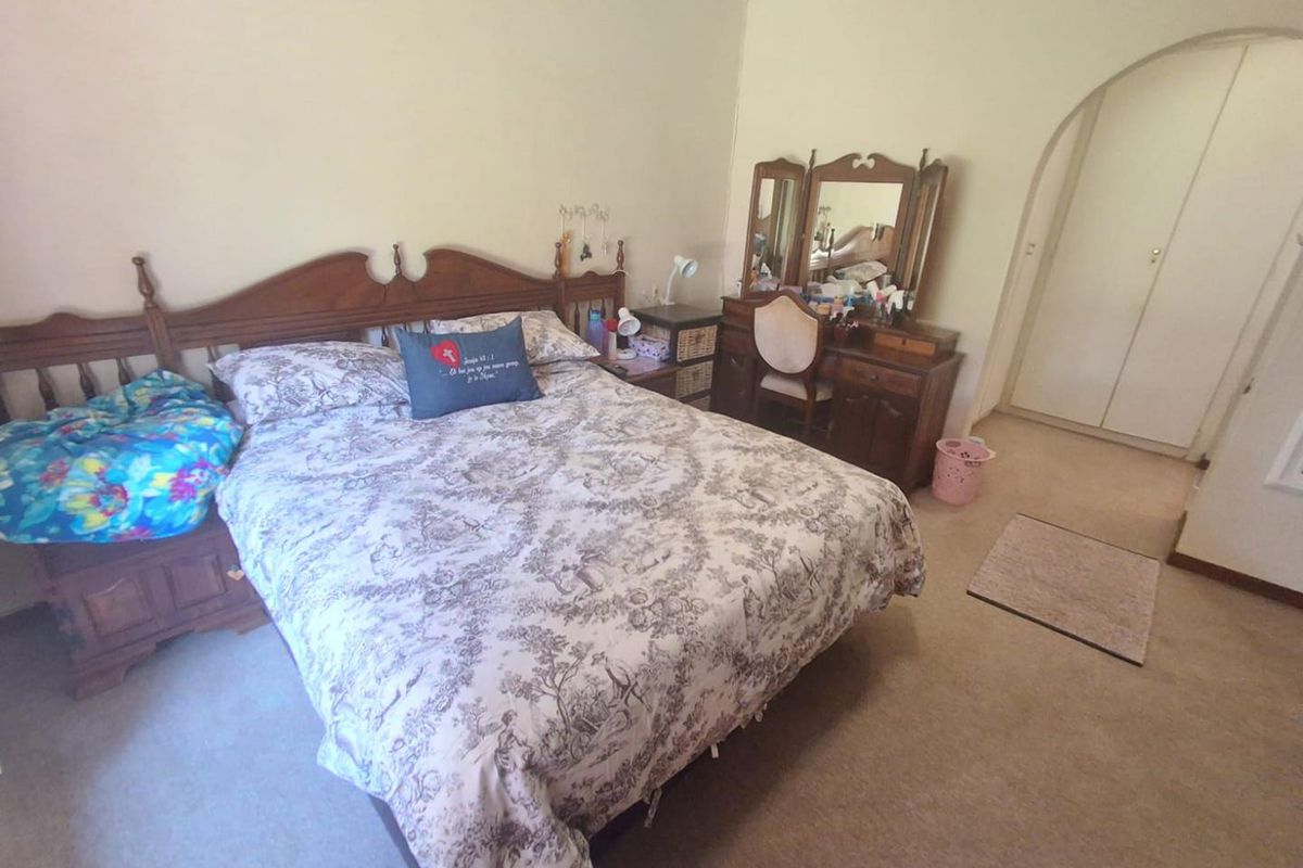 A carpeted bedroom featuring built-in cupboards and an arched doorway, offering a functional and neutral living space.