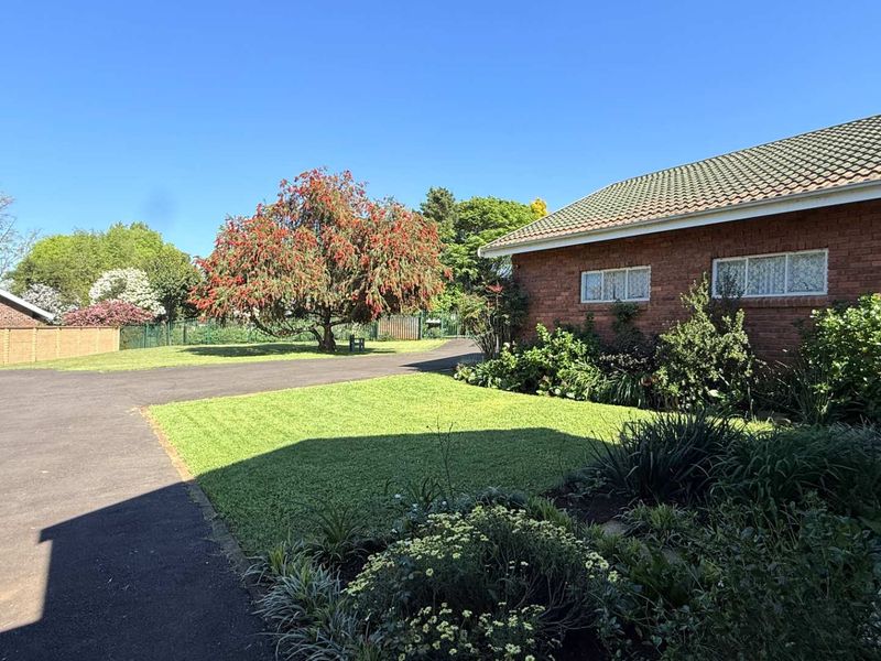 A view of the front exterior of the townhouse, featuring a brick facade, tiled roof, paved driveway, and a well-maintained garden area.
