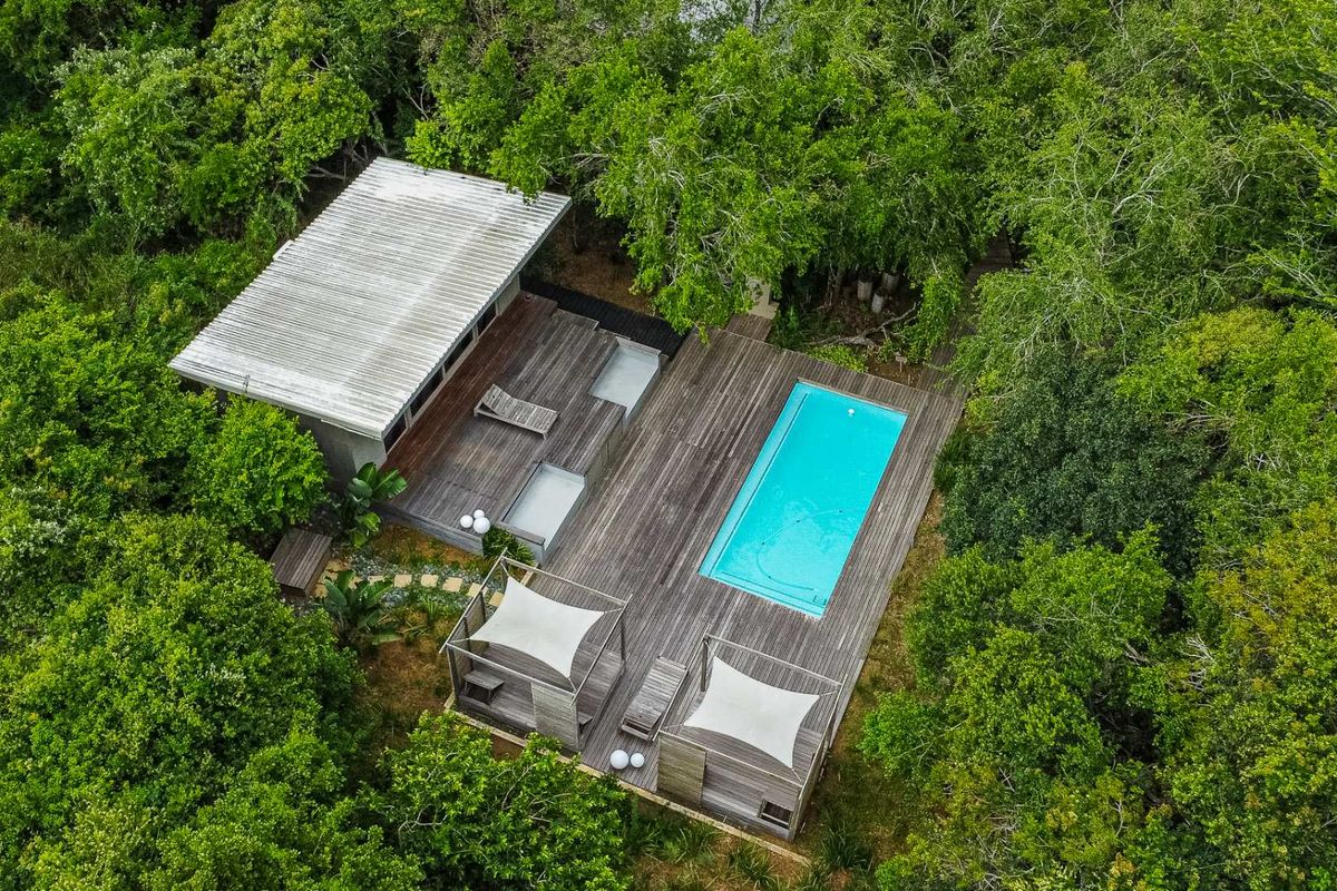 Aerial view of a secluded property featuring a swimming pool, extensive timber decking, and modern outdoor shade structures nestled within a lush forest setting.
