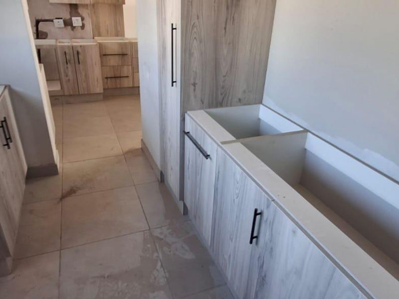 An unfinished kitchen area featuring light wood-grain cabinetry, tiled flooring, and prepared spaces for countertops and appliances.