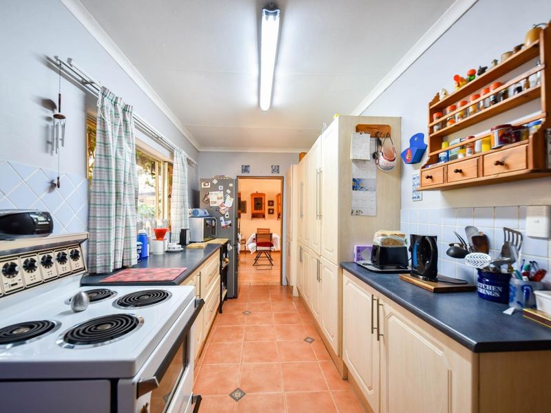 A functional galley-style kitchen featuring tiled flooring, ample built-in cabinetry, laminate countertops, and a tiled splashback, offering a practical layout for daily use.