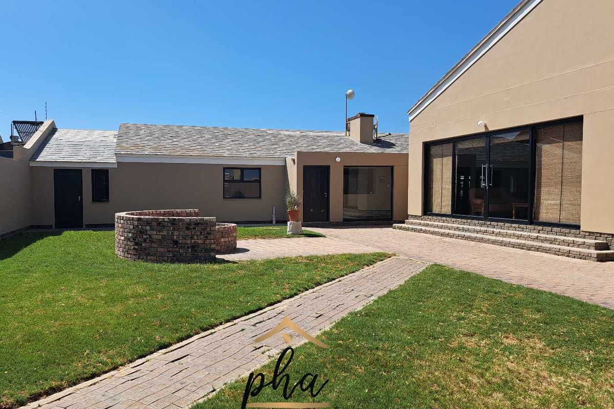 A well-maintained rear courtyard featuring a paved patio, brick fire pit, manicured lawn, and large sliding glass doors leading into the home.
