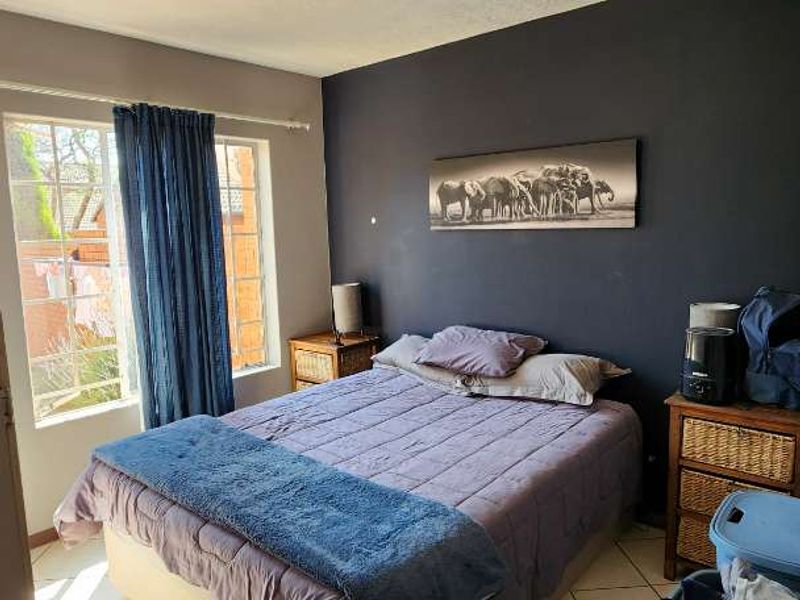 A bedroom featuring tiled flooring, a window with security bars, and a dark accent wall, providing a functional space with potential for cosmetic updates.
