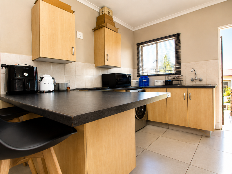 A functional kitchen featuring light wood cabinetry, dark laminate countertops, tiled backsplash, and direct access to an outdoor area.