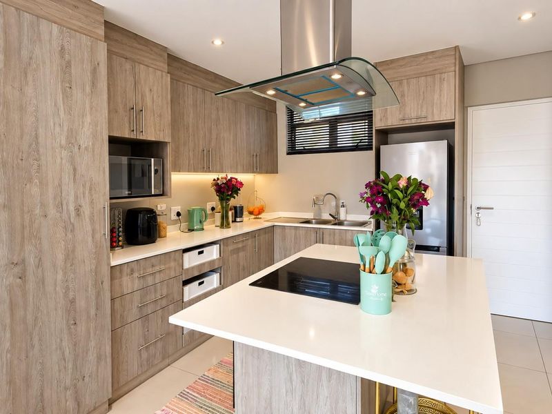Modern kitchen featuring wood-grain cabinetry, stone countertops, a central island with an integrated cooktop, and high-quality built-in appliances.