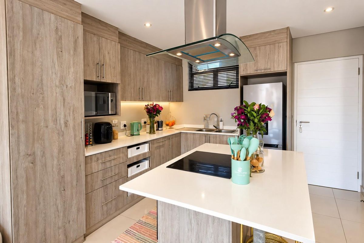 Modern kitchen featuring wood-grain cabinetry, stone countertops, a central island with an integrated cooktop, and high-quality built-in appliances.