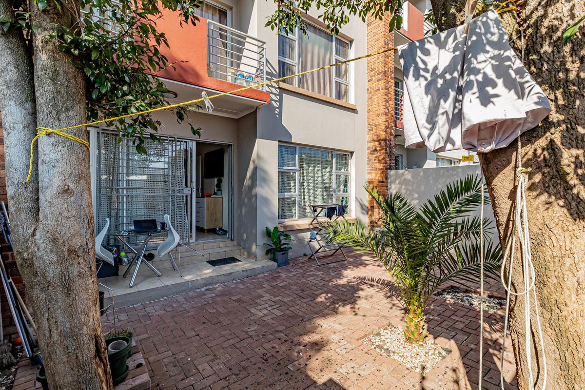 Rear view of the apartment building featuring a brick-paved patio area, security gate access, and an upper-level balcony.