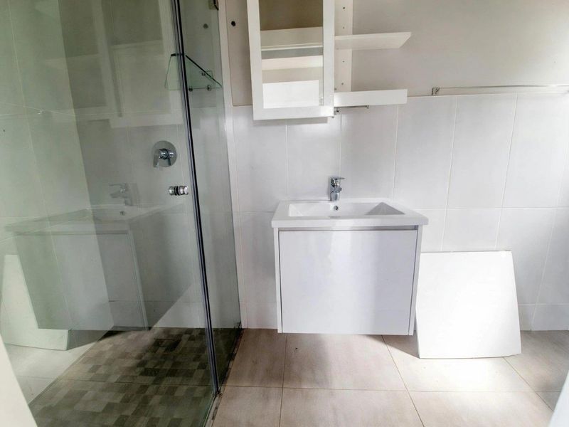 A functional bathroom featuring a glass shower enclosure, wall-mounted vanity with basin, and wall-mounted storage cabinet with neutral tiled finishes.