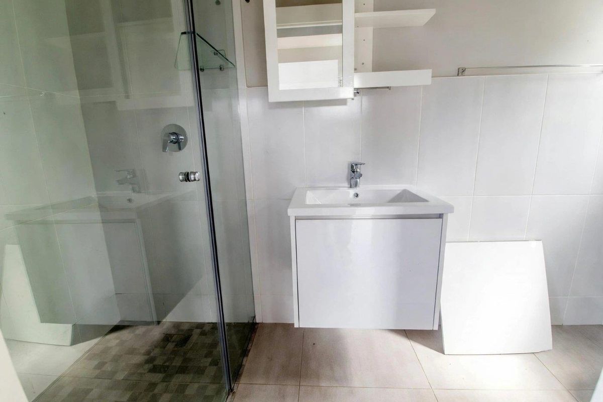 A functional bathroom featuring a glass shower enclosure, wall-mounted vanity with basin, and wall-mounted storage cabinet with neutral tiled finishes.