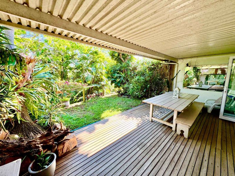 A covered outdoor patio featuring timber decking and a corrugated roof, overlooking a lush garden area with direct access to the interior.