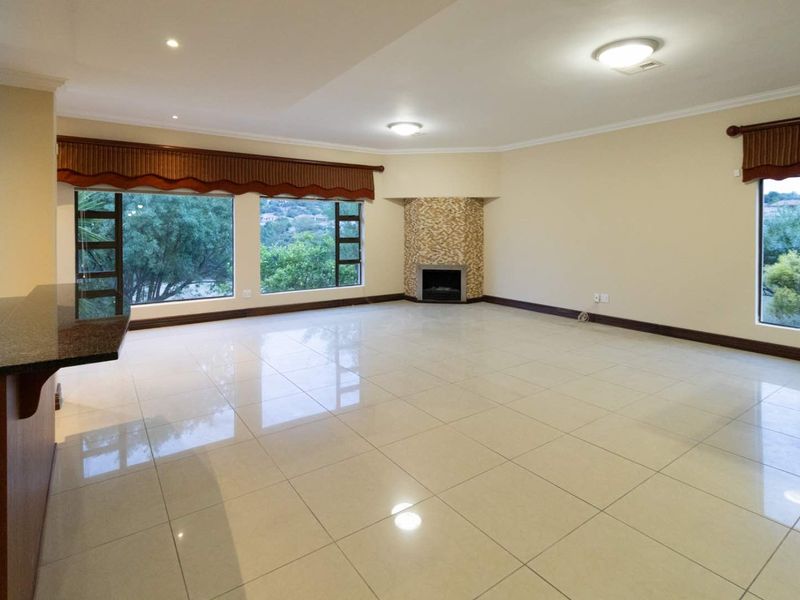 Spacious open-plan living area featuring polished tile flooring, a built-in fireplace with stone cladding, and large windows offering natural light and garden views.