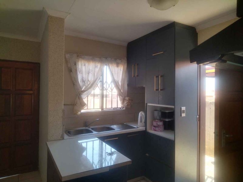 A functional kitchen featuring dark built-in cabinetry, a double sink with mixer tap, and a breakfast counter, with security bars on the window.