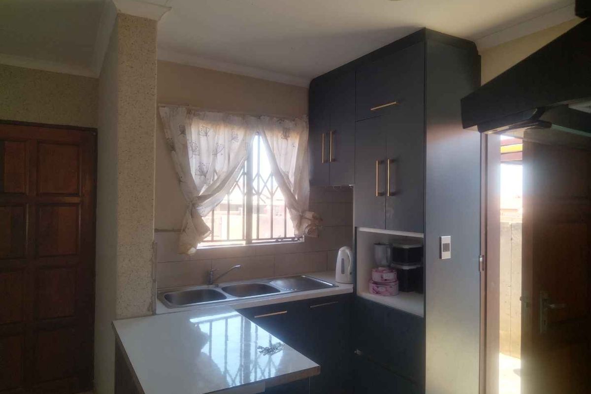 A functional kitchen featuring dark built-in cabinetry, a double sink with mixer tap, and a breakfast counter, with security bars on the window.