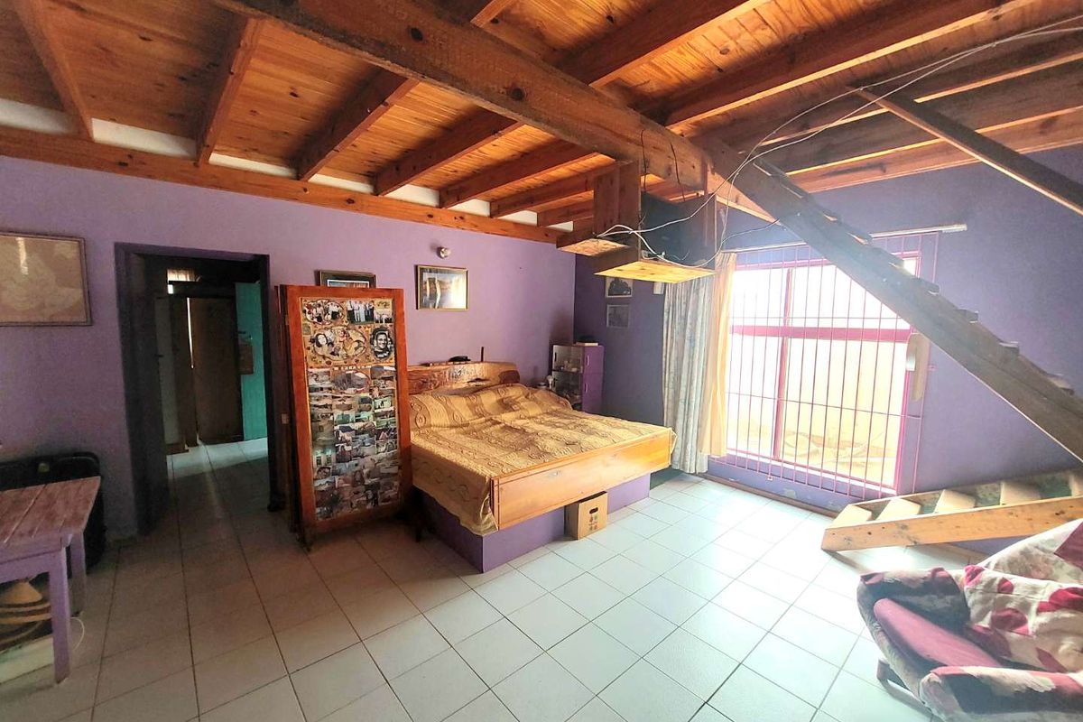 Spacious bedroom featuring exposed timber ceiling beams, tiled flooring, and an internal wooden staircase leading to an upper level.