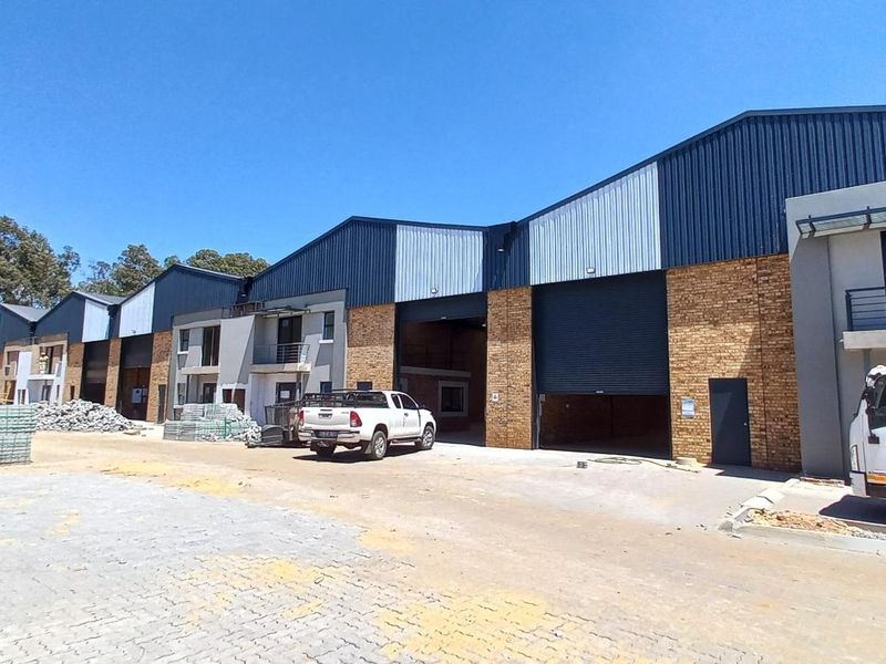 Front elevation of an industrial warehouse complex featuring multiple roller shutter doors, face brick and metal cladding finishes, and a paved yard area.