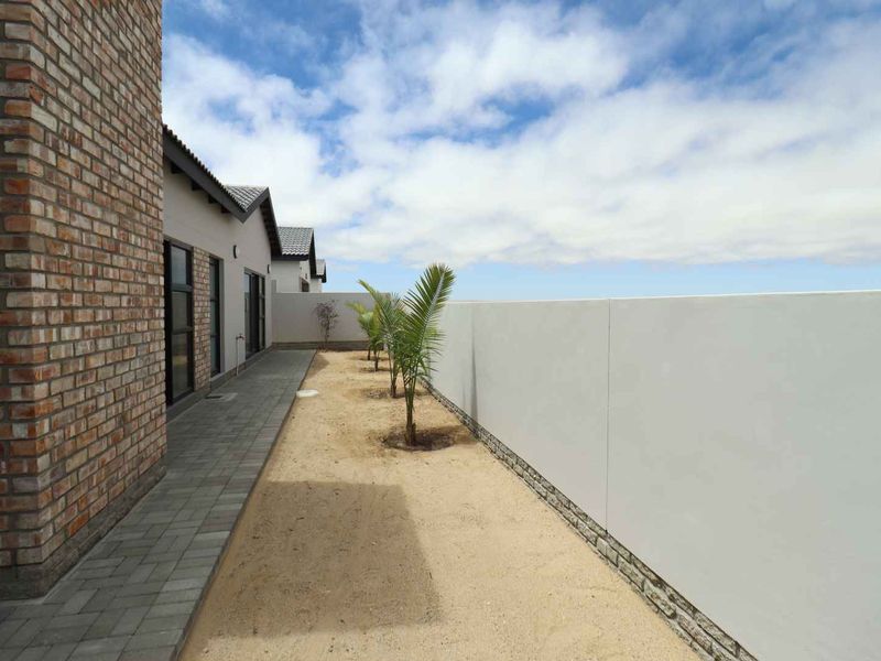 A side exterior view of the property featuring a brick facade, paved walkway, and a clean boundary wall.