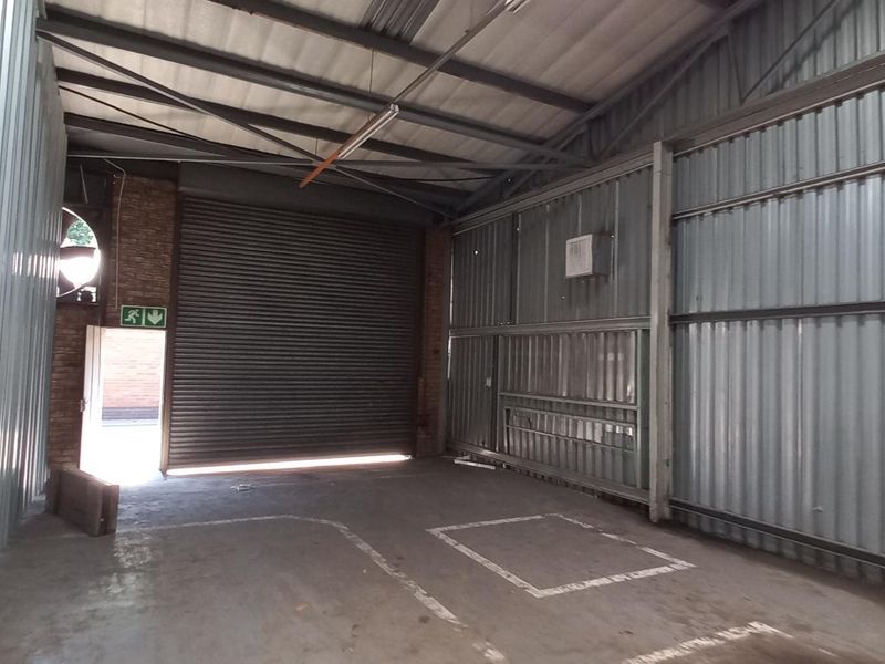 Spacious industrial garage featuring corrugated metal walls, a large roller shutter door, and exposed steel roof trusses with concrete flooring.