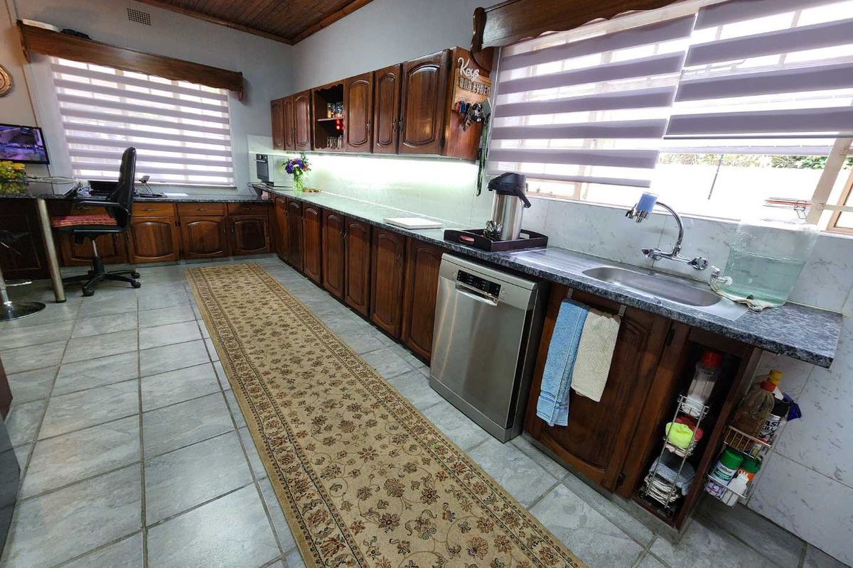 A functional kitchen featuring extensive timber cabinetry, stone-look countertops, a stainless steel dishwasher, and a double sink with tiled flooring.