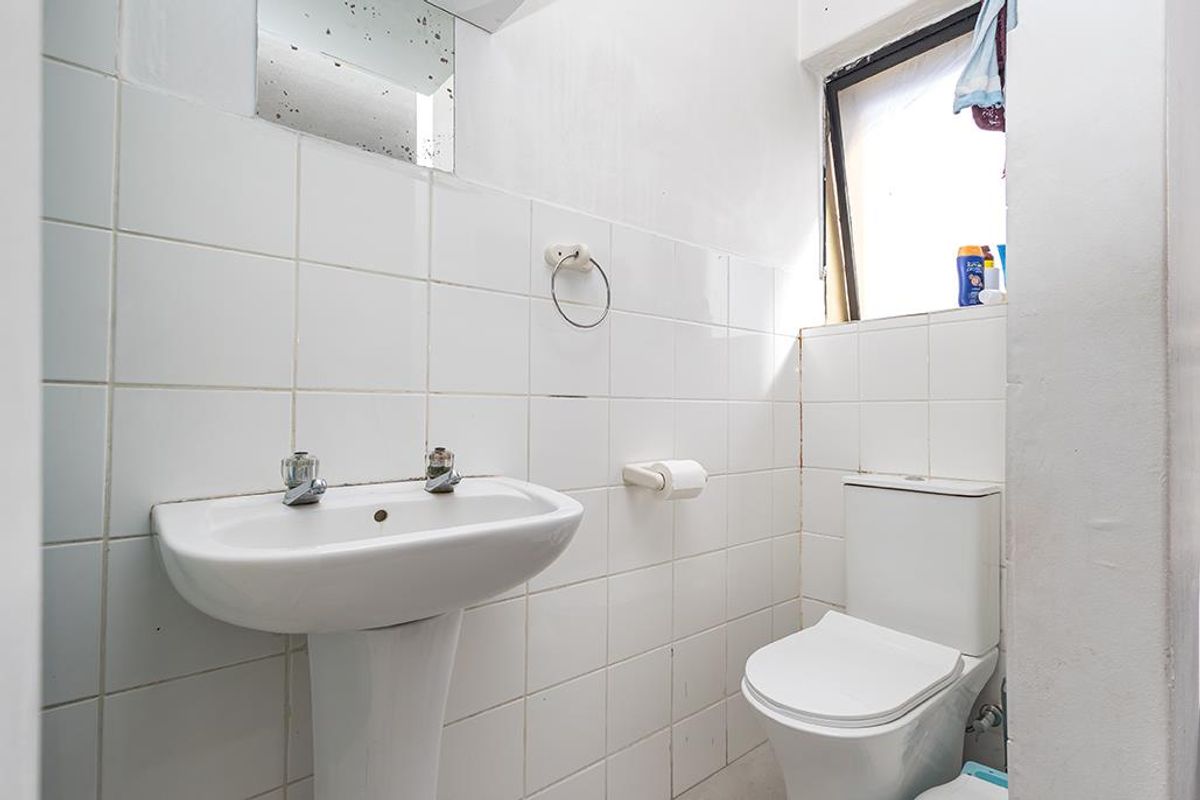 A compact bathroom featuring a pedestal basin, toilet, and white wall tiling. The space requires cosmetic updates to improve its overall condition.