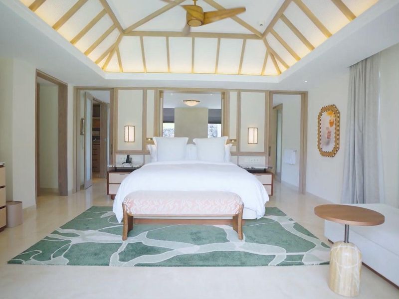 A spacious, well-appointed bedroom featuring a high vaulted ceiling with integrated fan, recessed lighting, and premium stone flooring.