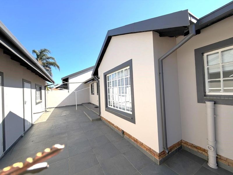A clean, paved rear exterior area featuring modern grey tiling, well-maintained exterior walls, and functional drainage systems.