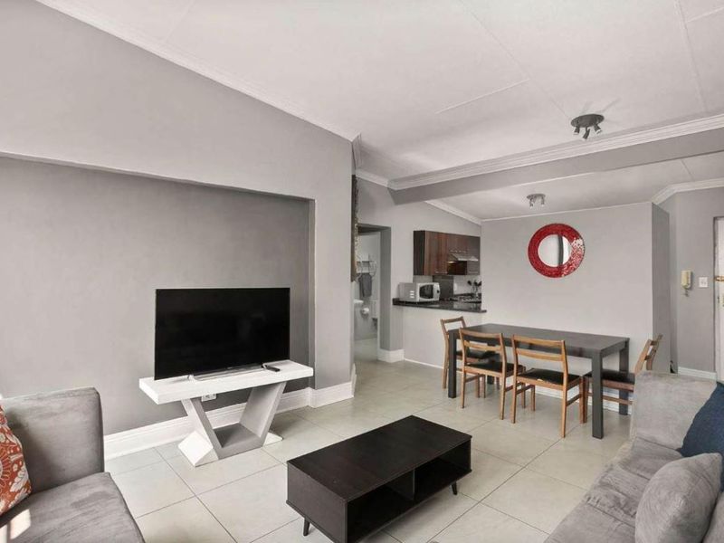 An open-plan living and dining area featuring neutral grey walls, tiled flooring, and a recessed wall niche, seamlessly connected to a functional kitchen space.