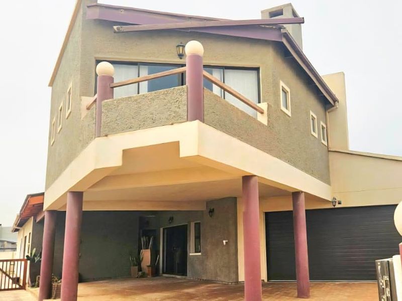 Front elevation of a multi-level house featuring a covered entrance, balcony, integrated garage, and paved driveway area.