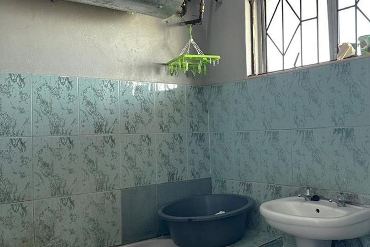 A dated bathroom featuring a pedestal sink, bathtub, and exposed wall-mounted water heater with vintage patterned wall tiles.