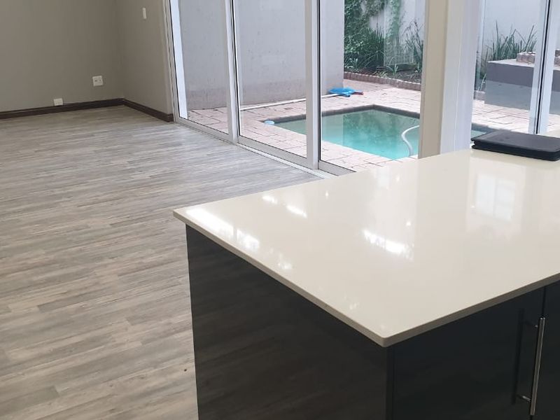 Open plan living area featuring a modern kitchen island with stone countertop, laminate flooring, and seamless access to an outdoor patio and swimming pool.