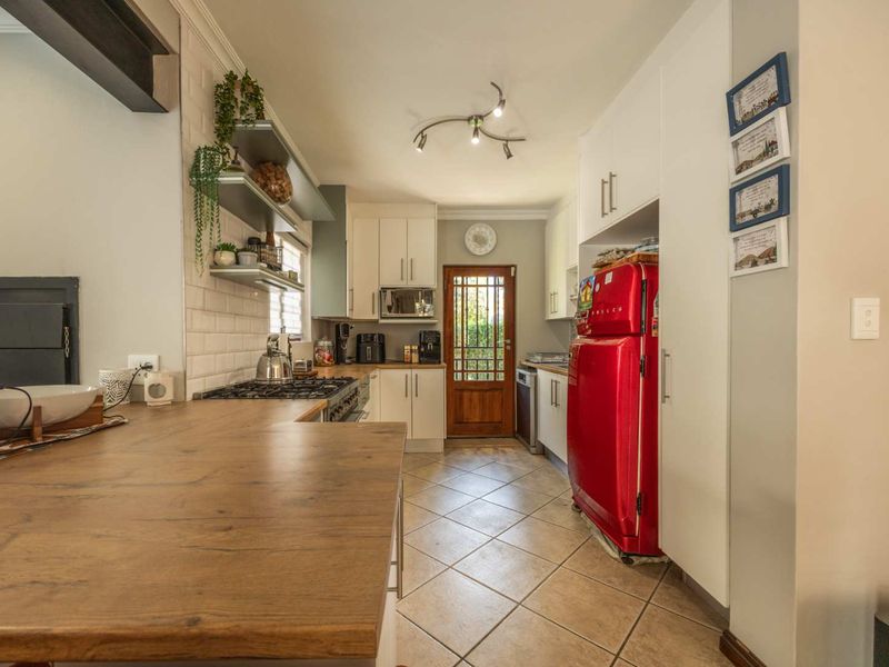 A well-maintained kitchen featuring white cabinetry, a gas hob, subway tile backsplash, and durable tiled flooring, leading to an exterior timber door.