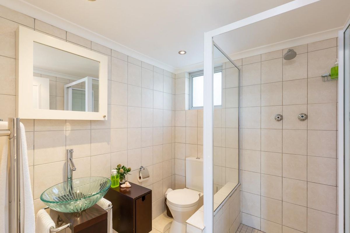 Modern bathroom featuring a glass vessel sink, walk-in shower with glass screen, and neutral wall tiling throughout.