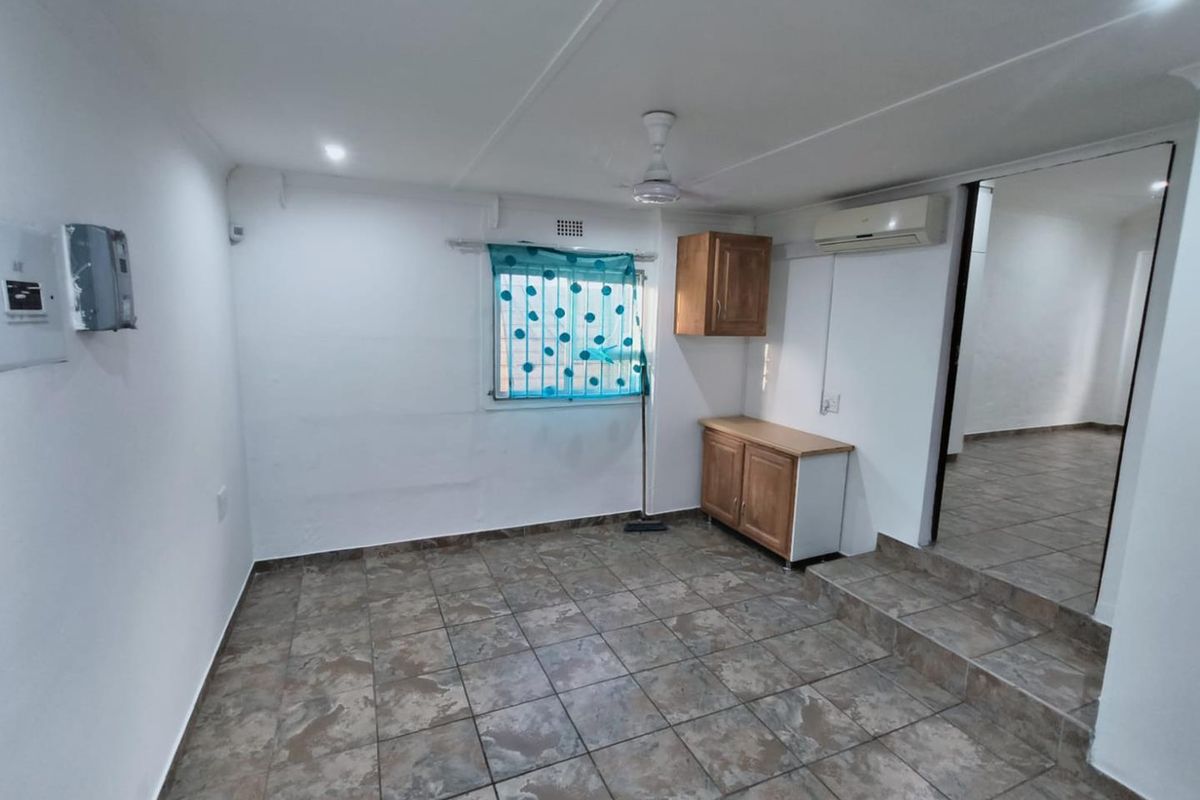A functional living space featuring tiled flooring, a ceiling fan, wall-mounted air conditioning unit, and built-in cabinetry.