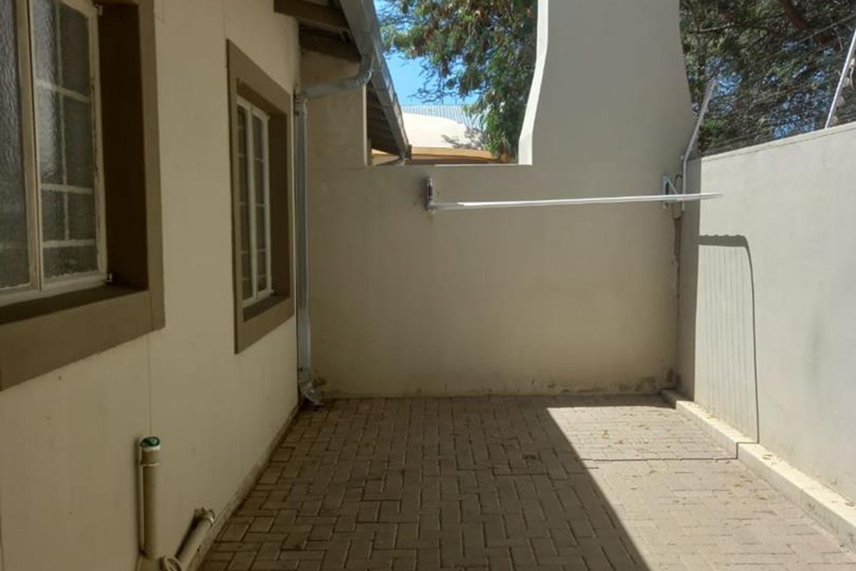 A paved rear courtyard area featuring a built-in chimney stack, exterior wall-mounted washing line, and drainage plumbing.