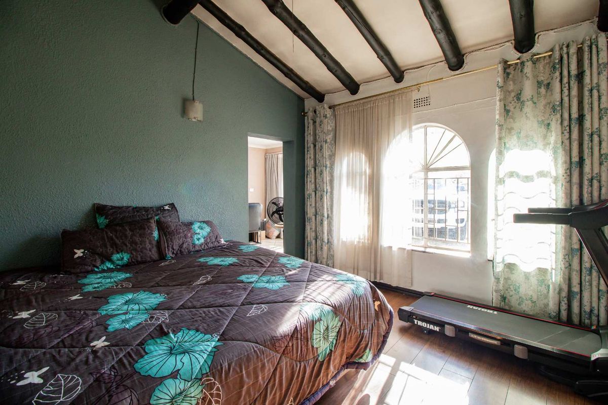 A bedroom featuring exposed timber ceiling beams, arched windows, and textured wall finishes, providing a rustic aesthetic.
