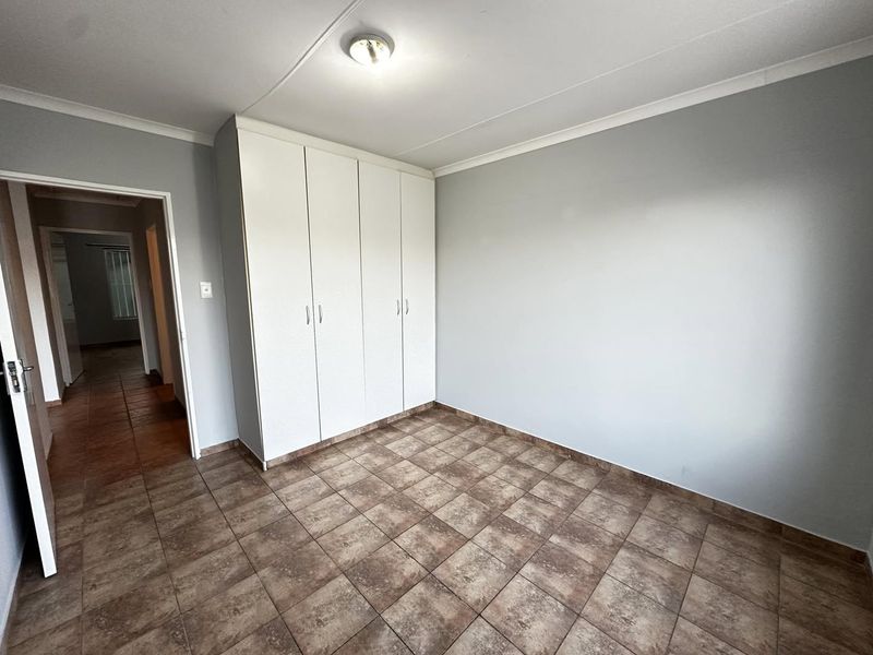 A clean, empty bedroom featuring neutral wall paint, ceramic tiled flooring, and built-in white cupboards.