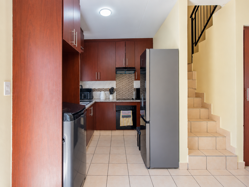 Compact kitchen featuring dark wood cabinetry, mosaic tile backsplash, and tiled flooring, conveniently located adjacent to the staircase.
