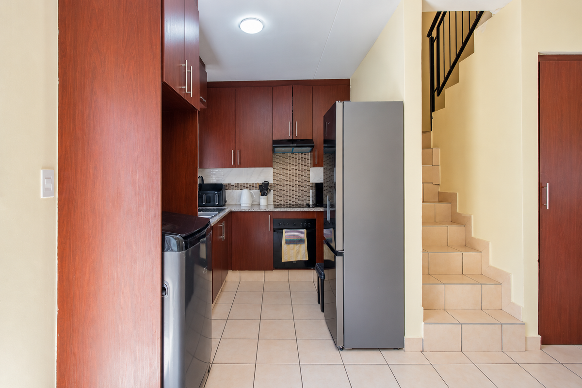 Compact kitchen featuring dark wood cabinetry, mosaic tile backsplash, and tiled flooring, conveniently located adjacent to the staircase.