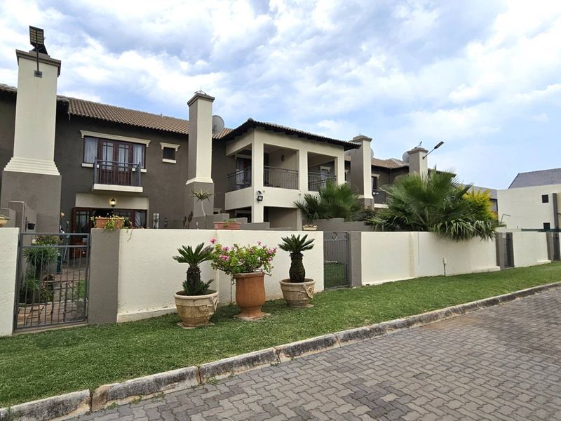 Front elevation of a multi-unit townhouse complex featuring tiled roofs, chimney stacks, private balconies, and secure boundary walls with gated access.