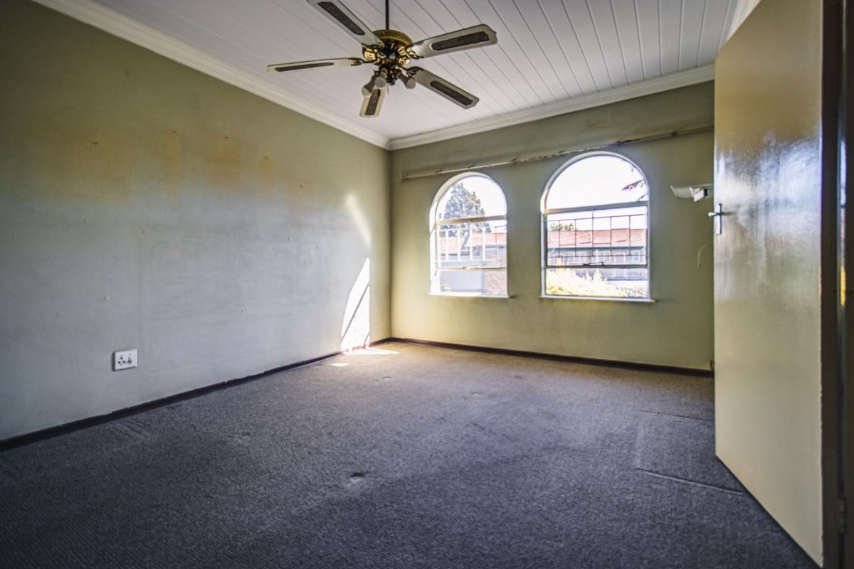 An empty bedroom featuring arched windows, a ceiling fan, and carpeted flooring, offering a blank canvas for renovation and personalization.