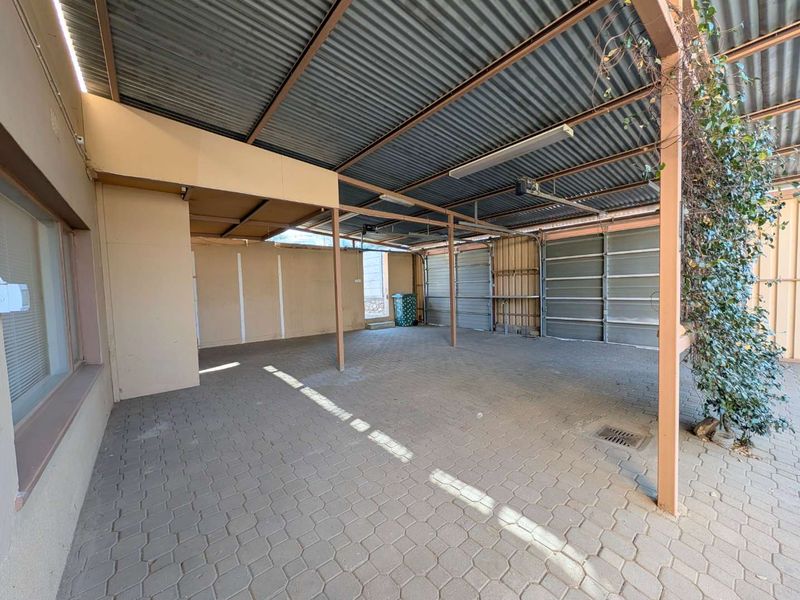 A spacious, open-sided garage area featuring paved flooring, a corrugated metal roof, and multiple garage door bays.