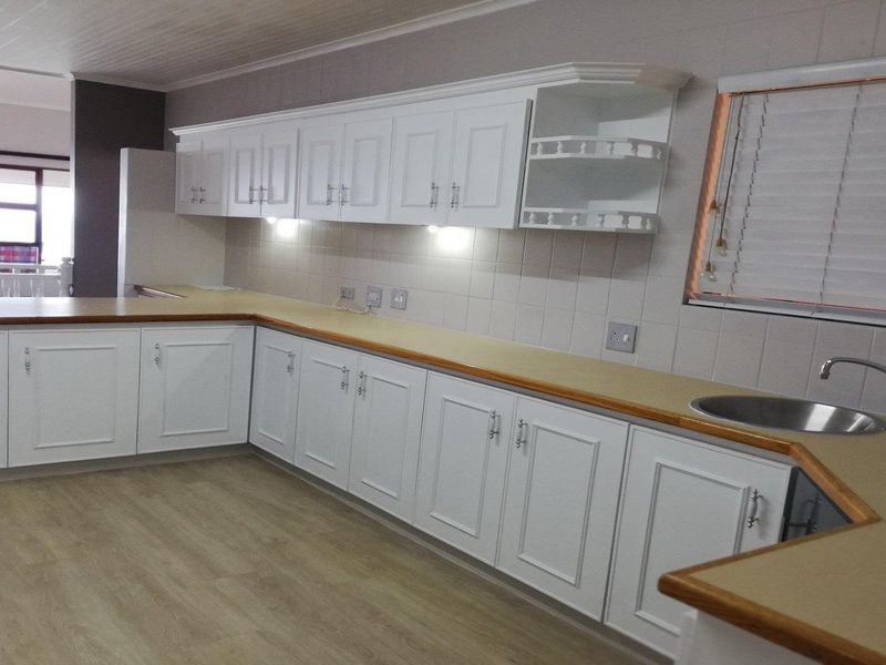 A clean, functional kitchen featuring white cabinetry, laminate countertops, tiled backsplash, and modern laminate flooring, offering a bright and well-maintained workspace.