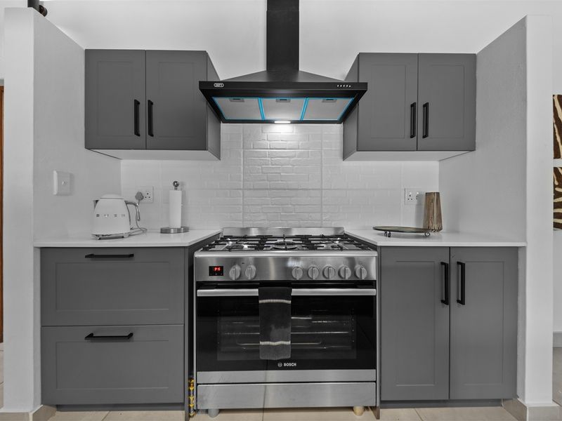 Modern kitchen featuring dark grey cabinetry, stainless steel gas stove with oven, extractor fan, and white subway tile backsplash.
