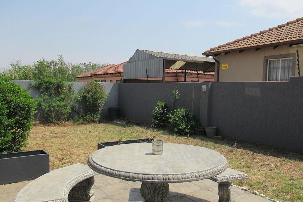 A private rear garden featuring a paved patio area, perimeter boundary wall, and established landscaping.